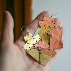 Ručně vyrobené výrazné náušnice z mědu a mosazi - sešité pohyblivými spojami z různých tvarů do velkých obdélníků - foceno na dlani 